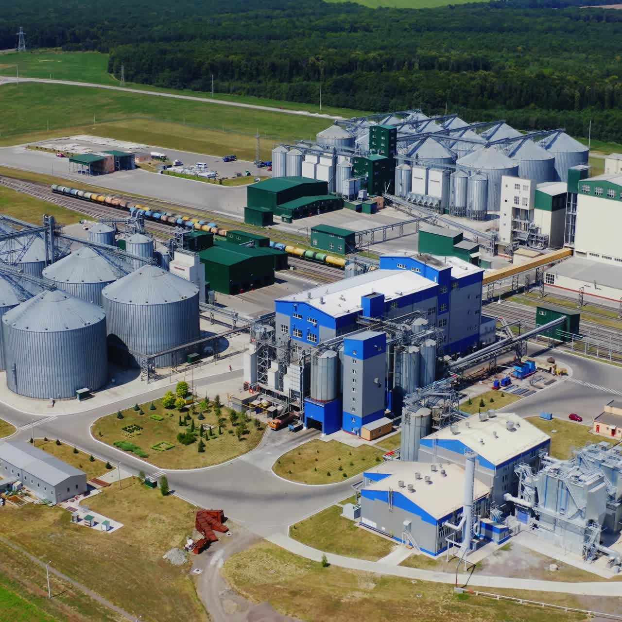 Elevators among green nature. Modern agricultural zone for grain storage. Granary on field. Steel tanks for storing cereals. Aerial view.
