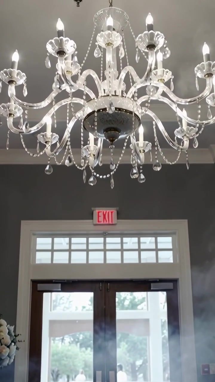 Video verticale: La telecamera si inclina rivelando un lampadario sopra porte a vetri con l'insegna USCITA per una cerimonia.