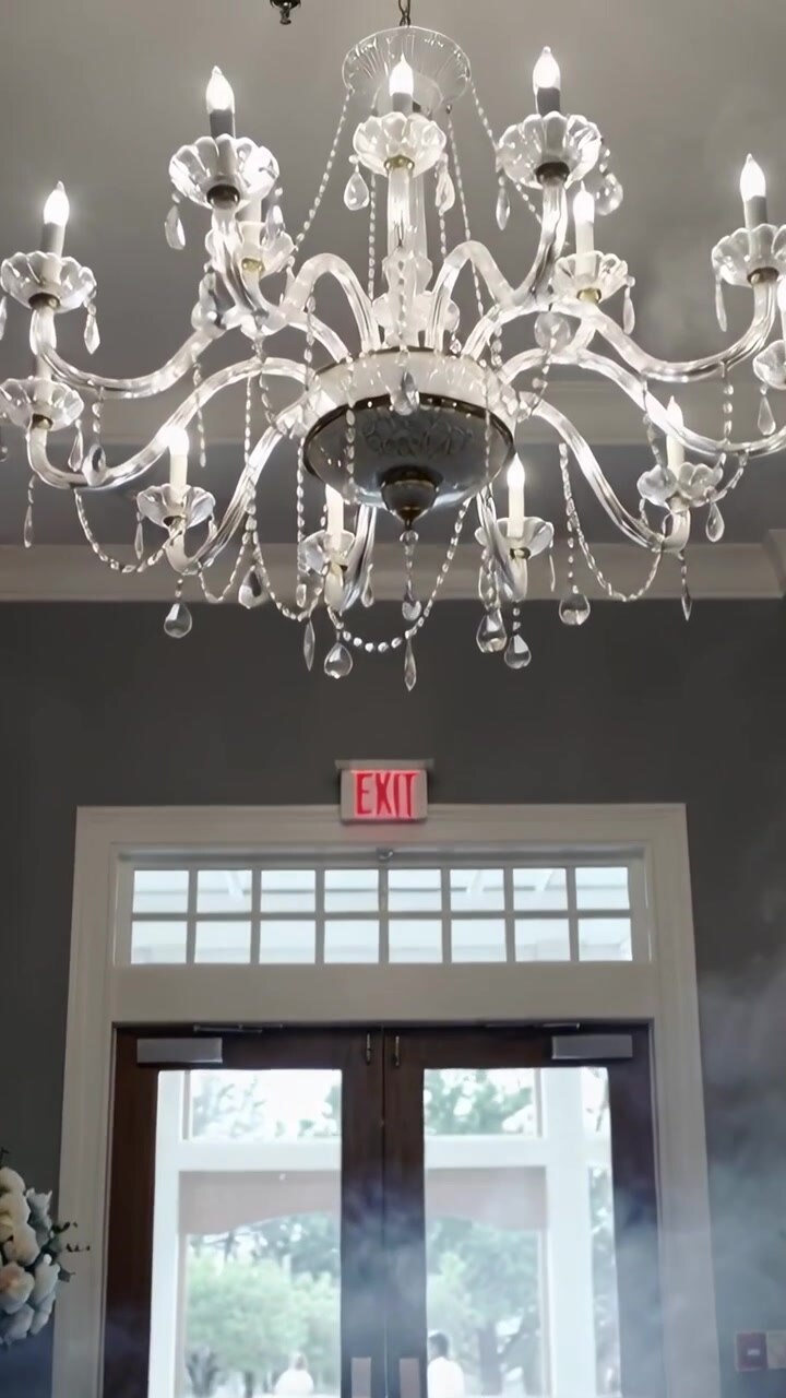 Video verticale: La telecamera si inclina rivelando un lampadario sopra porte a vetri con l'insegna USCITA per una cerimonia.