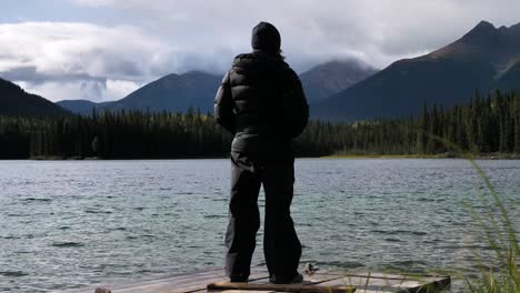 Person-on-Jetty-Looking-Out-at-Lake,-Forest-and-Mountain-Landscape-in-Canada,-Daydreaming-Scene,-Handheld