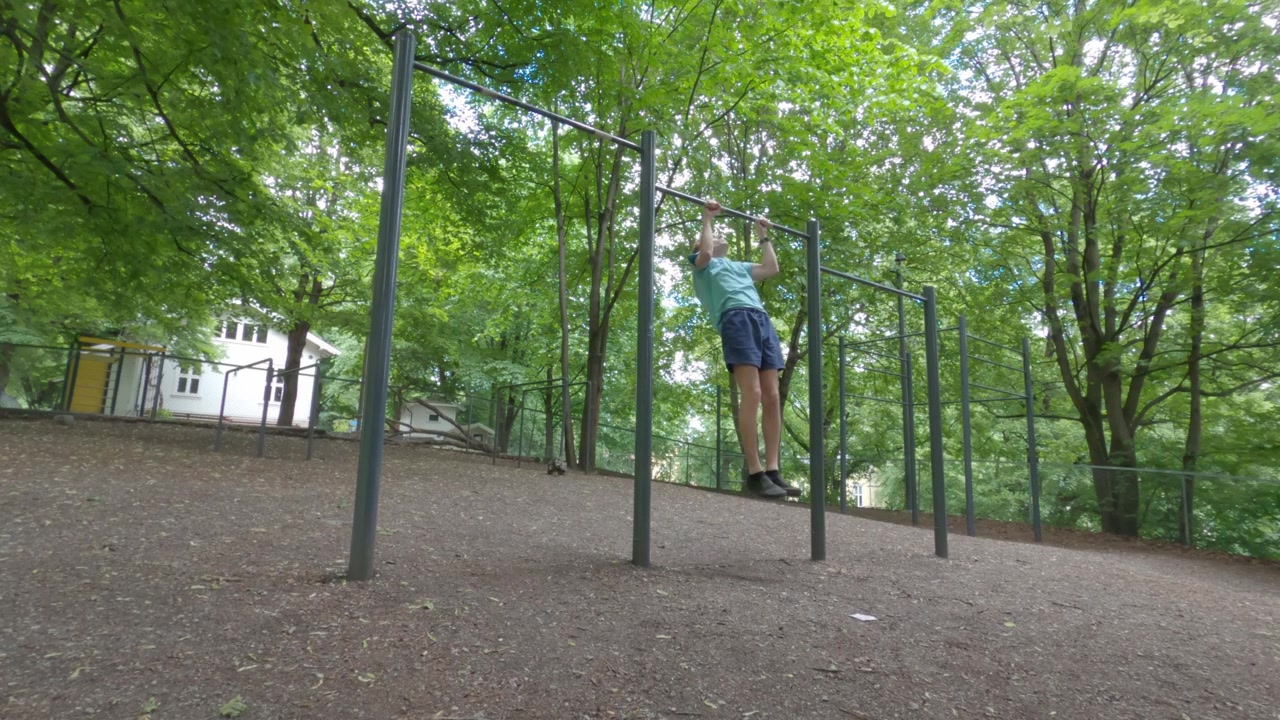Young man walks through St. Hanshaugen calisthenics park in Oslo on a summer day jumping up to do a pull up on bars