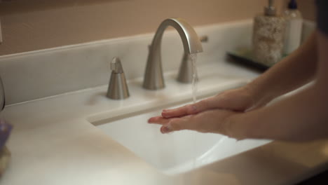 Medium-close-up-shot-of-a-male-washing-his-hands-in-a-white-sink-beige-bathroom