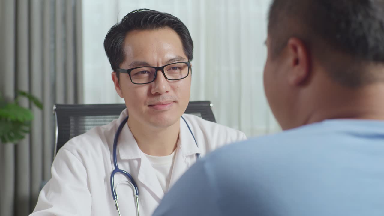 アジア人の男性医師が頭を振って診療所の太った男性患者に耳を傾けています
