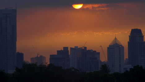 Time-Lapse-Golden-Sunset-Behind-Clouds,-City-Skyscrapers-Skyline-In-Silhouette