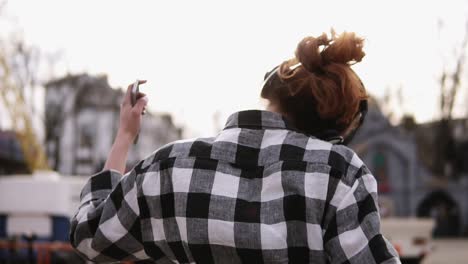 backside, slow motion shooting of a girl in expressive dance, wearing headphones. emotionally whirling her head. in a plaid shirt and mobile phone in her hand