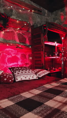 Romantic bedroom at Christmas. Cozy bed and Christmas garland on a wall. Candlesticks with red candles. Christmas decor in the room. Red lighting. Vertical video
