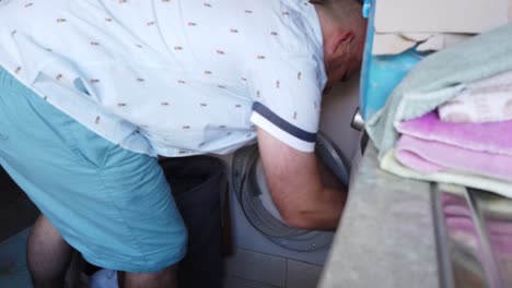 hombre en la lavandería poniendo una carga de ropa en una lavadora de carga frontal antes de agregar detergente líquido en la máquina y encenderla