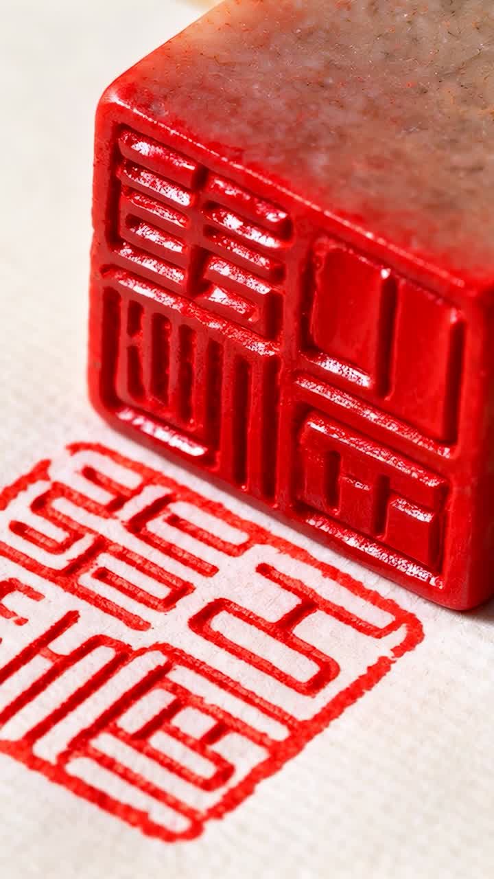 Vertical video: Pressing stone seal angled above textured paper to transfer red pigment, copy space