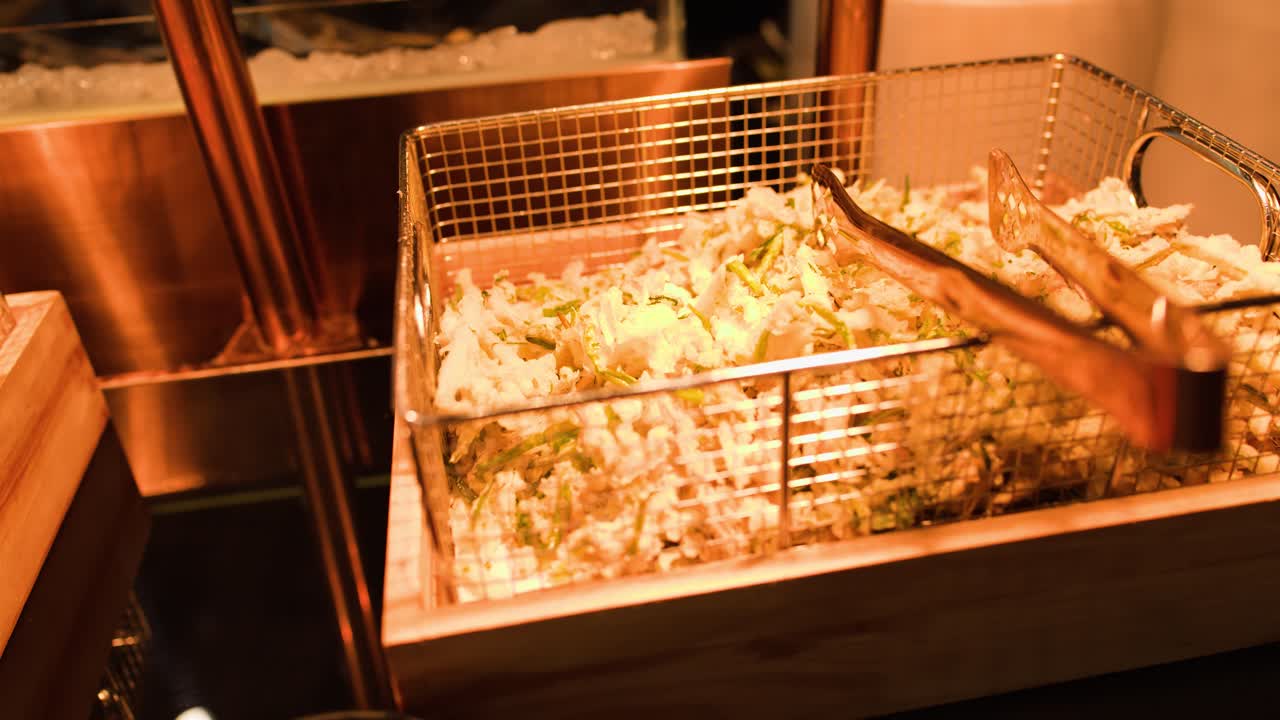 Ladle scoops crispy tempura from buffet basket under warm lighting, close-up, slight camera movement