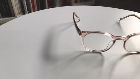 Modern-eyeglasses-in-light-colour-lie-on-a-white-table,-bright-glasses-frame,-slow-motion-footage