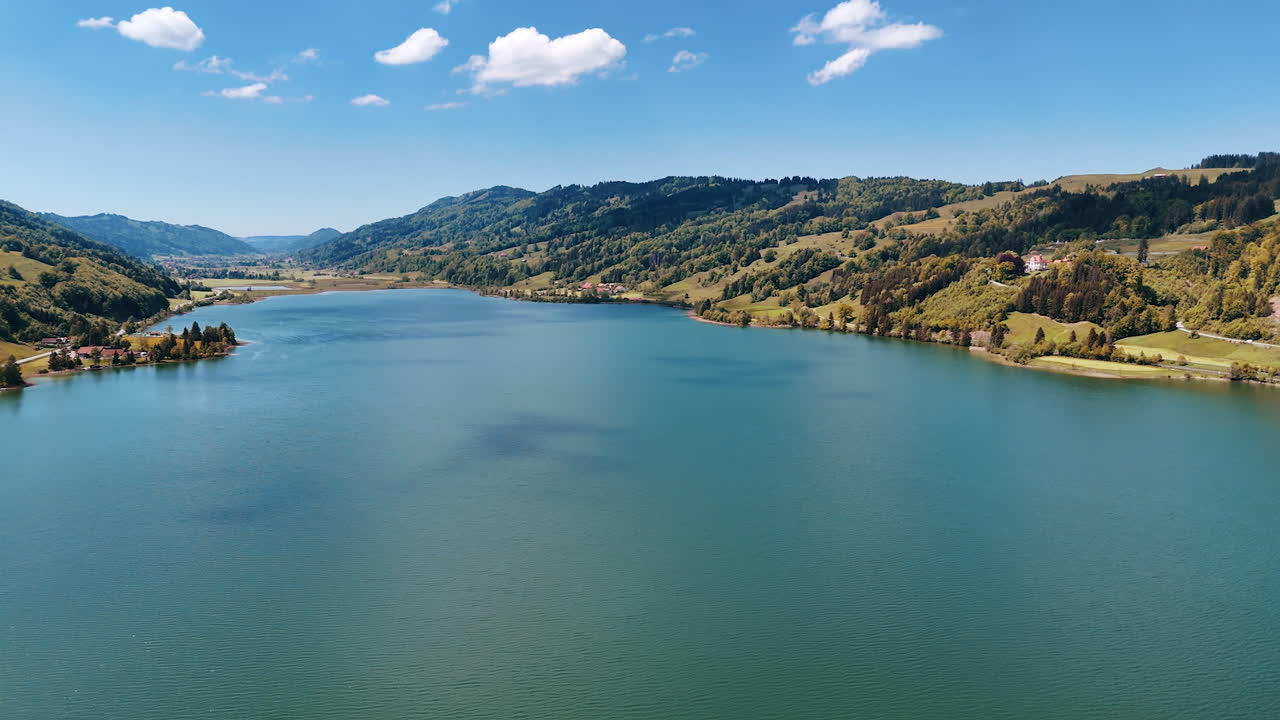 Footage above the peaceful waterscape of the lake among the mountainous banks. Green forests grow on the rocks. Aerial view.