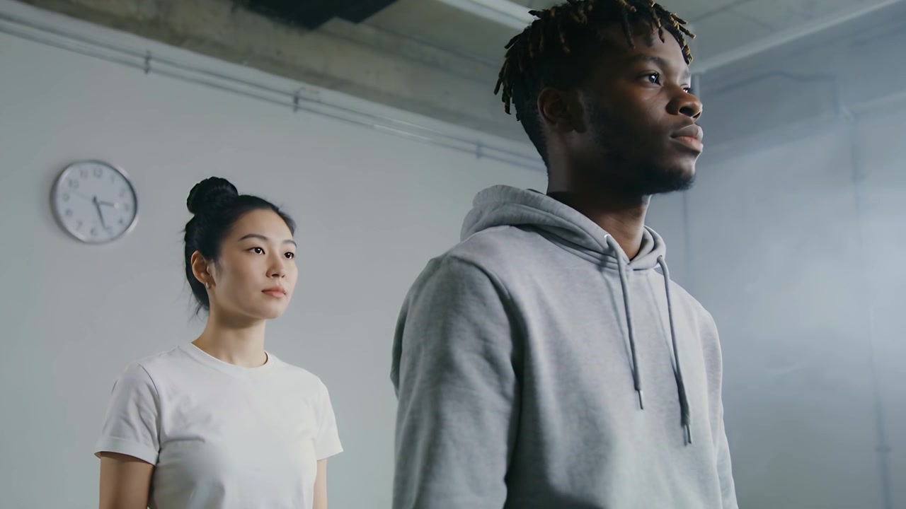 Holding pose, two peers rehearsing in studio while camera tightening focusing on male hoodie, clock