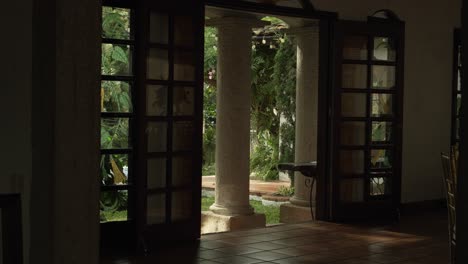 open colonial style doors reveal serene courtyard with stone columns and lush greenery. real estate.