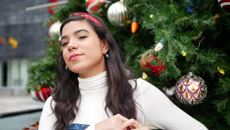 una mujer alegre comprando regalos navideños en la ciudad con un árbol decorado con adornos y luces festivas