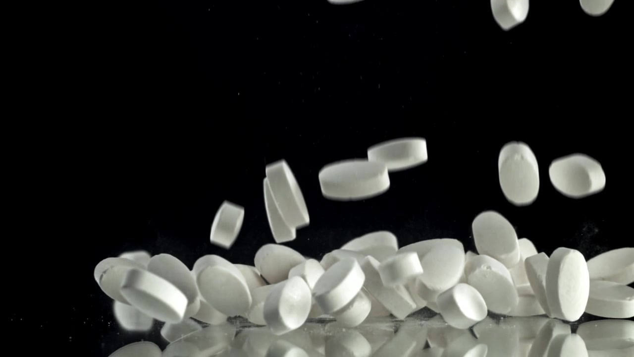 White Pills Falling in Slow Motion on Black Reflective Surface