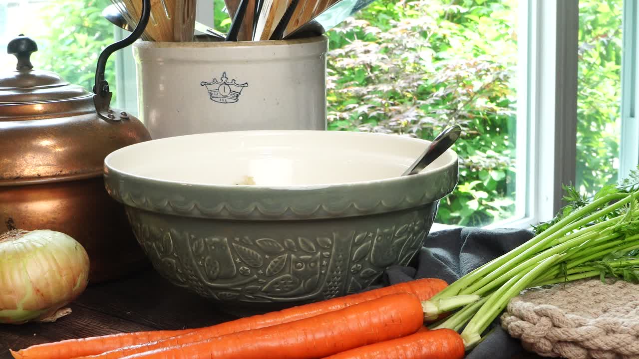 Making meatballs for Italian Wedding Soup. Adding herbs and spices with a spoon in a big green ceramic bowl on a counter in the kitchen. Fresh vegetables like carrots and onions on the counter.
