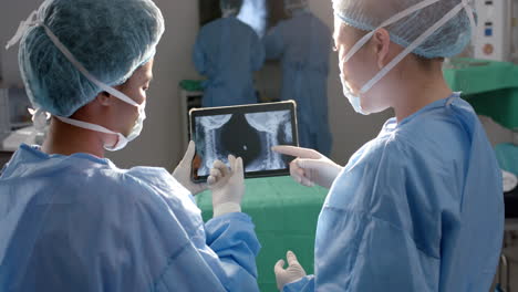 Diverse-female-surgeons-looking-at-x-ray-scans-on-tablet-in-operating-theatre,-slow-motion