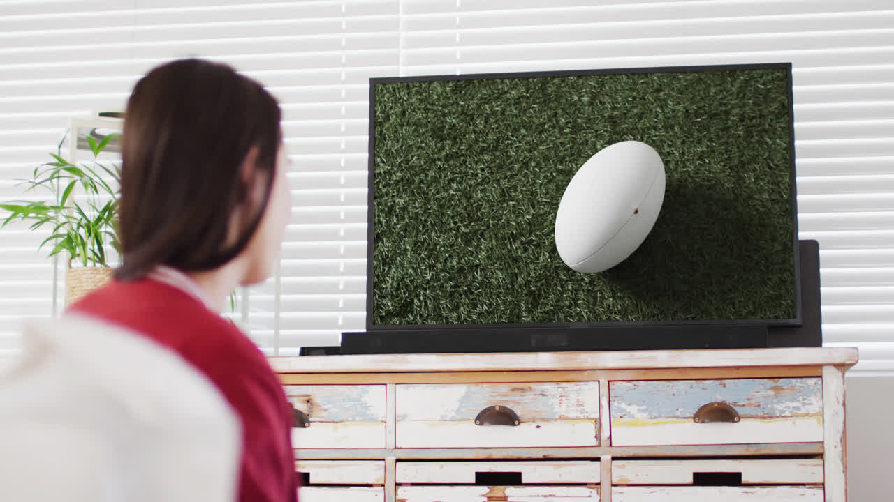 스크린 에 있는 경기장 에서 럭비 공 을 들고 tv 를 보는 백인 여자