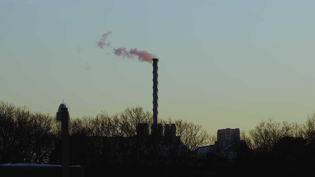 Steam billowing from tall exhaust stack after sunset, during mid-winter near Saco, Maine. Wide shot. Slow motion.