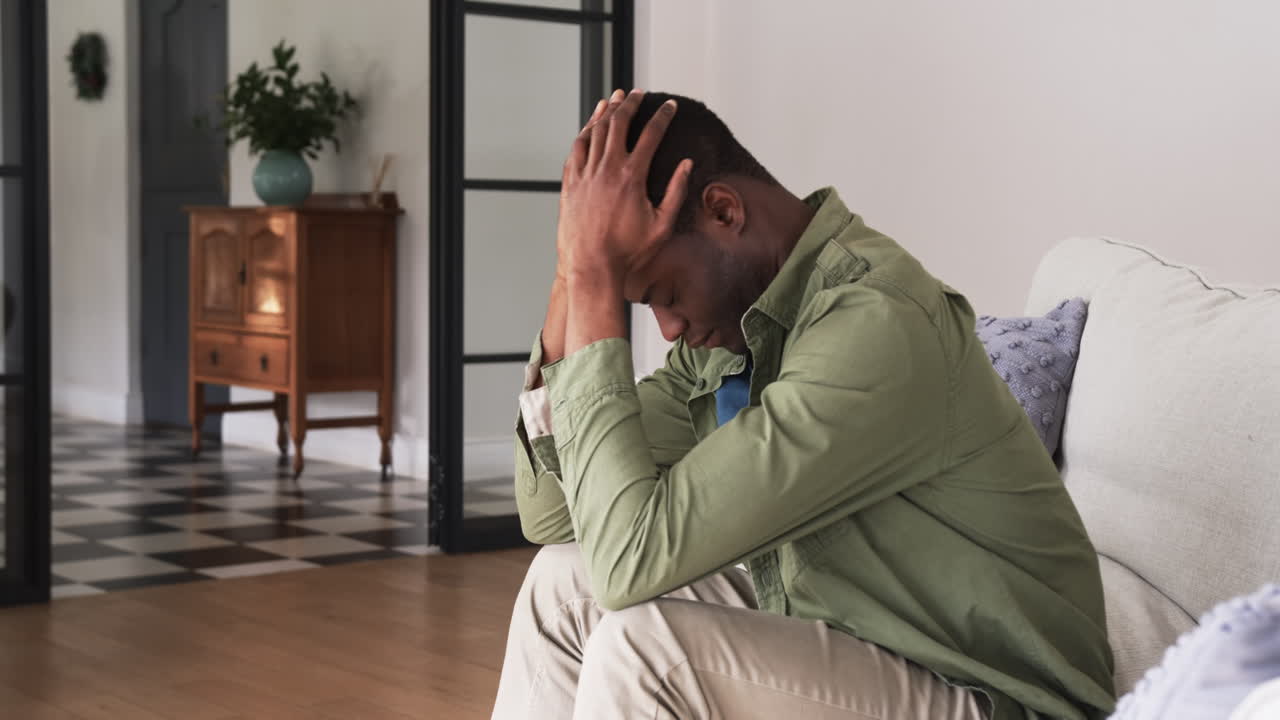 Man sitting on couch at home, looking stressed and holding head in hands, copy space