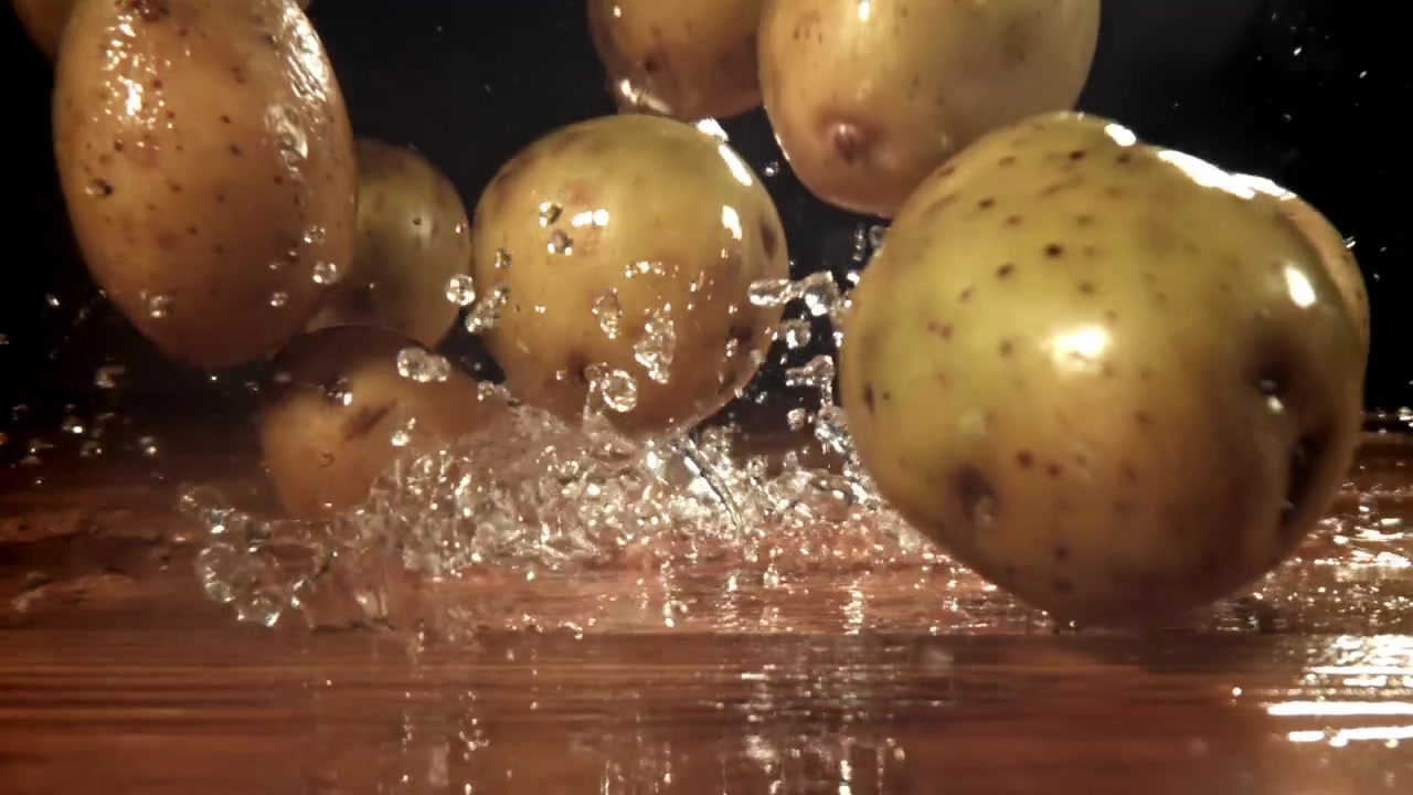Patate fresche che cadono e schizzano acqua su una superficie di legno.