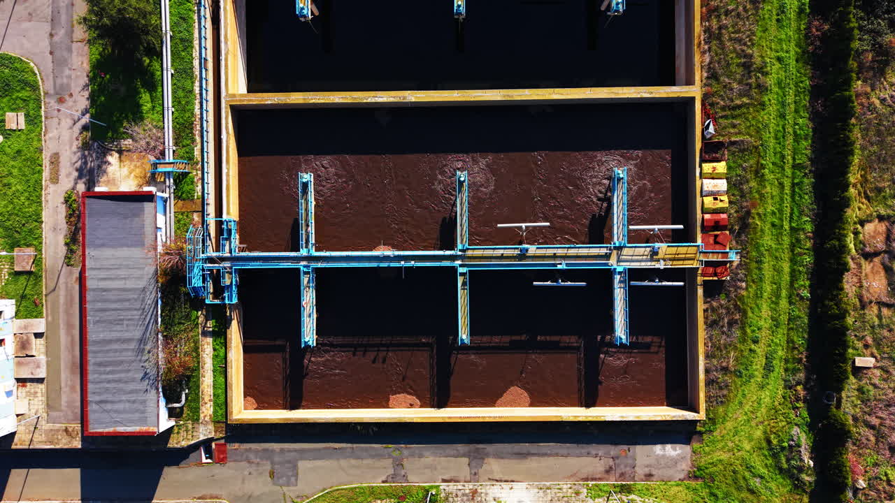 Industrial basin with brown water and metal bridge structures for processing. Overhead aerial view of rectangular wastewater aeration tank