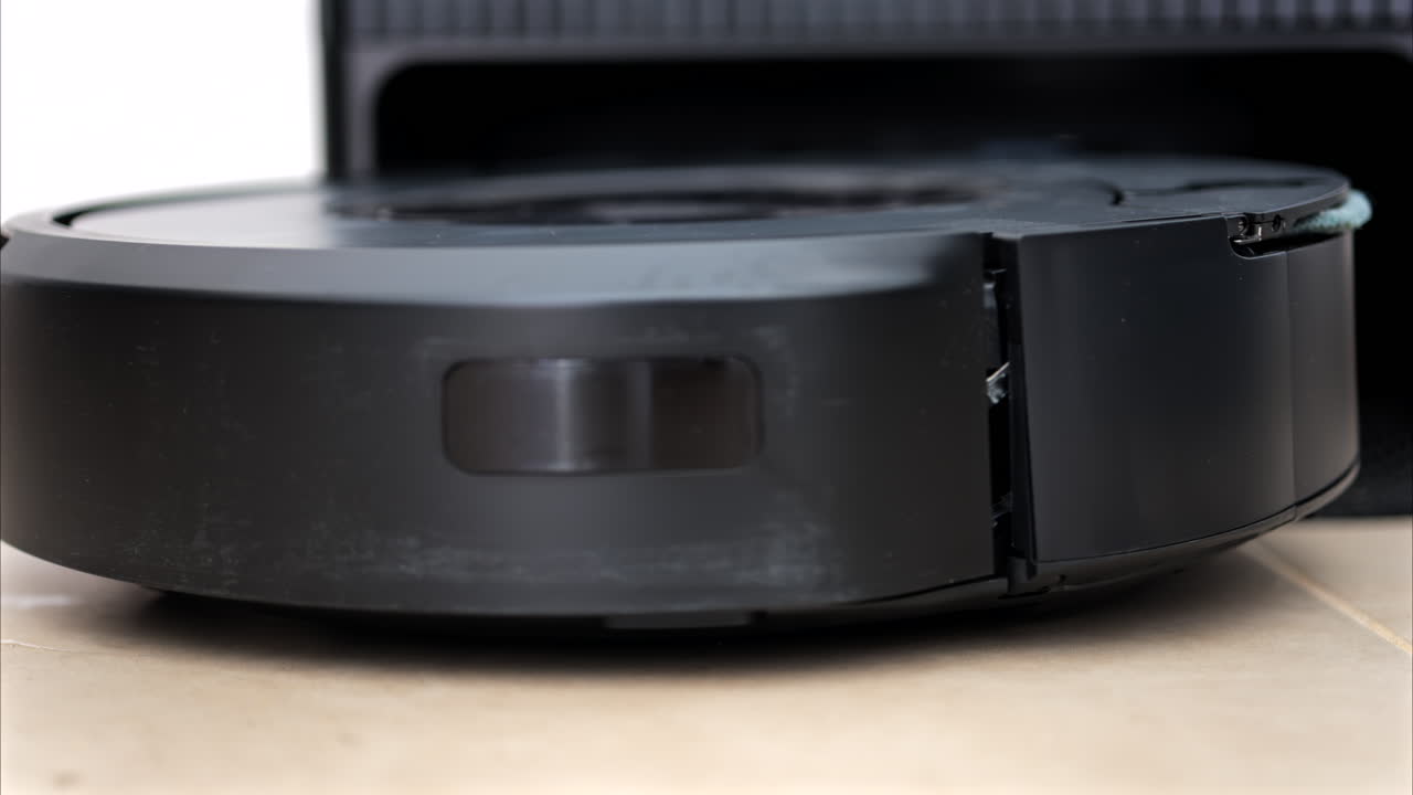 Close up of a black robot vacuum cleaner moving and rotating on the floor tiles