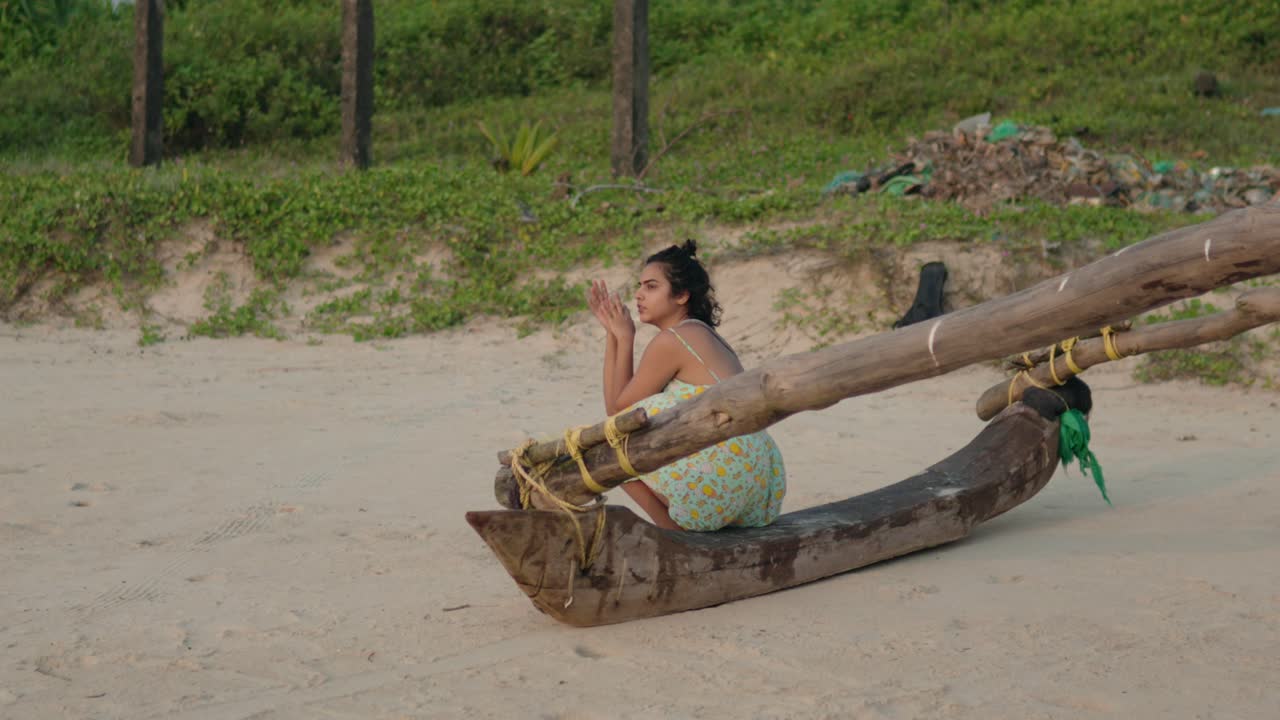 disparo de viaje lateral que captura a una joven india sentada en un barco de pesca indio tradicional en una playa tropical, ofreciendo un vistazo de la serena escena costera