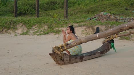 Lateral-traveling-shot-capturing-a-young-Indian-woman-seated-on-a-traditional-Indian-fishing-boat-at-a-tropical-beach,-offering-a-glimpse-of-the-serene-coastal-scene