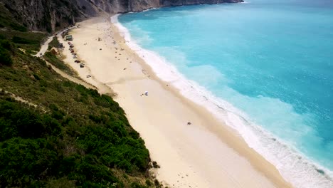 Drone-panning-from-the-right-to-the-left-side-of-the-frame-doing-a-slight-pedestal-shot-while-showing-the-jagged-cliffs-and-the-crystal-clear-blue-waters-of-the-Mediterranean-Sea-in-Greece