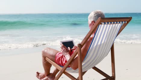 retired old man using tablet while lying on deckchair