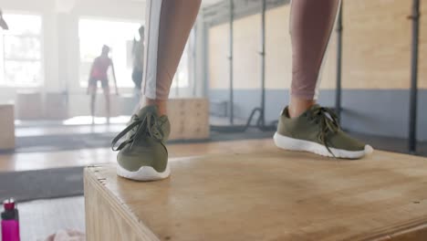 low section of unaltered woman jumping on box, training at fitness class in gym, slow motion