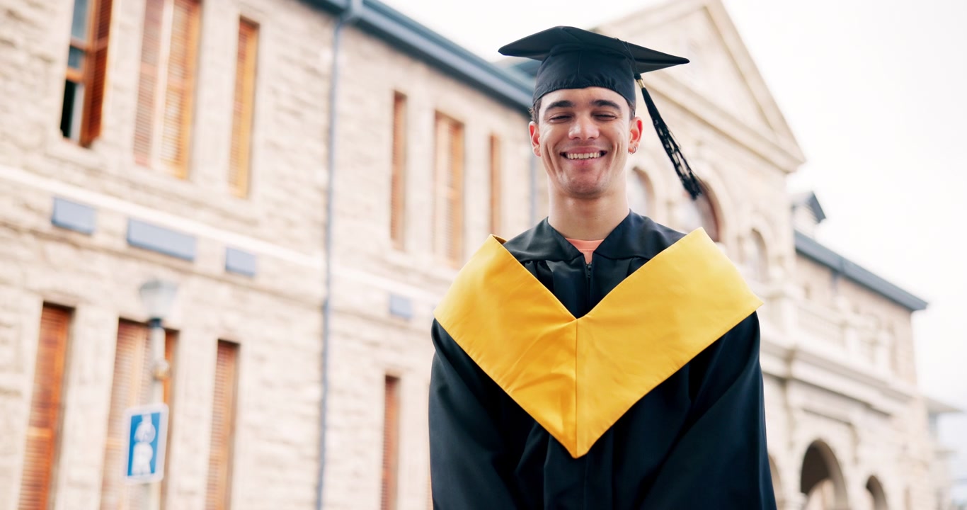 Giovane uomo felice in toga di laurea in piedi fuori dall'edificio universitario