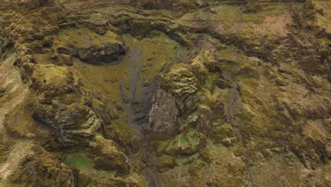 fotografía aérea de formaciones rocosas escarpadas y cubiertas de musgo en brókarjökull, islandia, que muestran acantilados escarpados y texturas de tierra en un paisaje estéril