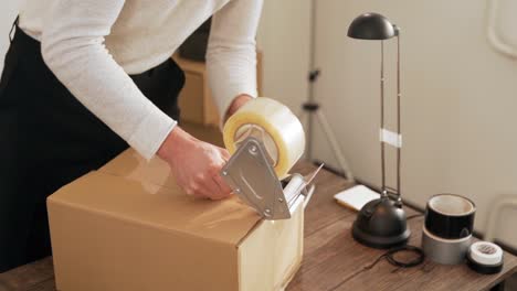 close-up of a man's hand packing a cardboard box with a packing gun