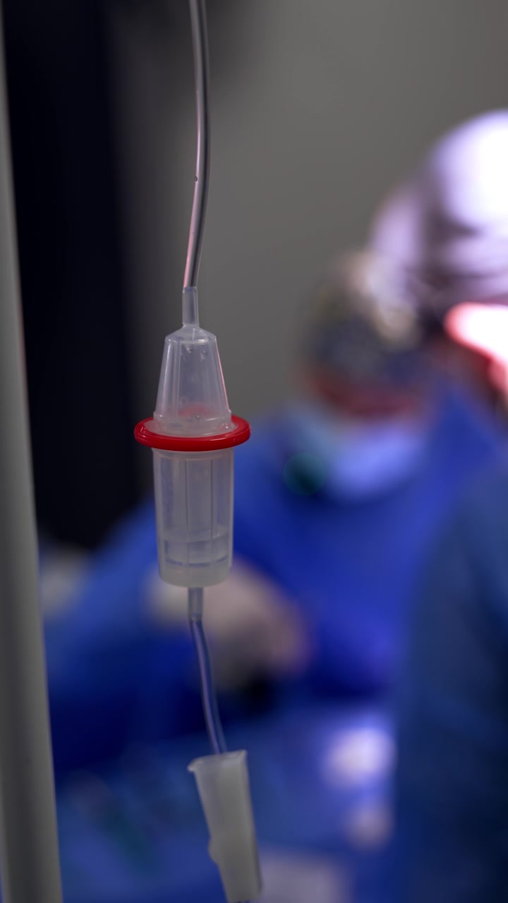 Flebo con il medicinale che gocciola all'interno. Primo piano. Immagine sfocata di medici che lavorano sullo sfondo. Video verticale.