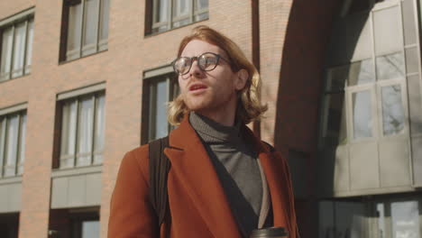 cheerful businessman walking in city and drinking to go coffee