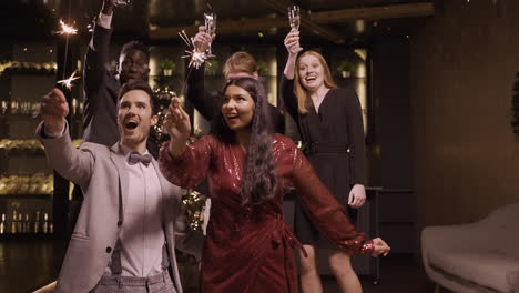 group of friends wearing stylish clothes celebrating new year eve while holding sparkles and champagne glasses, then confetti falls as they jump for joy and kiss