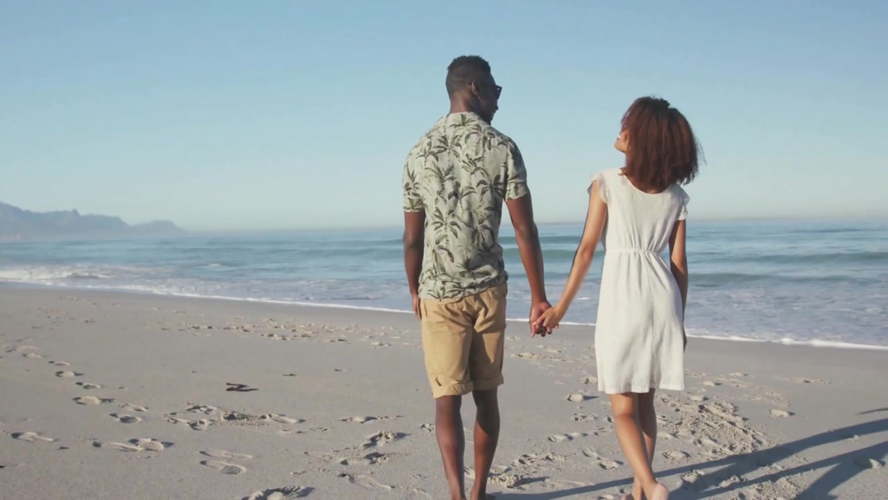 Couple walking hand in hand on beach, showcasing business branding as flag overlay dissolving