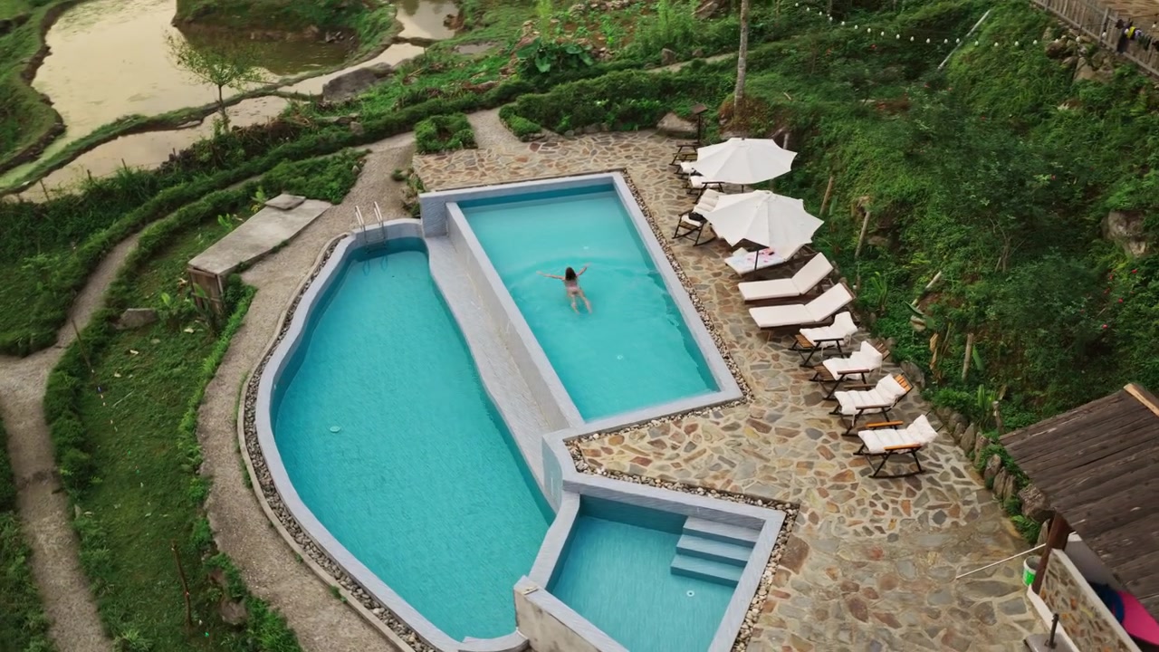 Kvinde ved swimmingpoolen på et økolodge-resort i de naturskønne bakker ved Sapa, Vietnam. Droneoptagelse, nedadgående bevægelse.