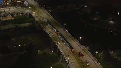 Vista-Aérea-Siguiendo-Un-Tranvía-Que-Pasa-Un-Puente-En-El-Centro-De-Houston,-Noche-En-Texas,-Estados-Unidos