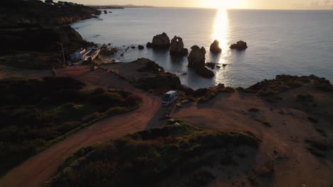 Aerial-view-motorhome-parked-Praia-dos-Arrifes-glowing-sunlit-sunrise-Portugal-shoreline