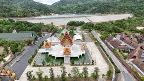 drone footage captures a serene buddhist temple in phuket, thailand, surrounded by lush greenery and a tranquil river