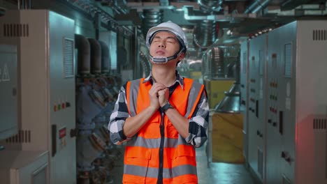 asian male engineer with safety helmet pray for something while standing in engine control room, work of electrical generators