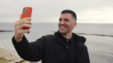 Un-Hombre-Se-Divierte-Y-Hace-Una-Mueca-Tonta-Mientras-Se-Toma-Selfies-Y-Crea-Historias-En-Las-Redes-Sociales-Mientras-Está-En-La-Playa