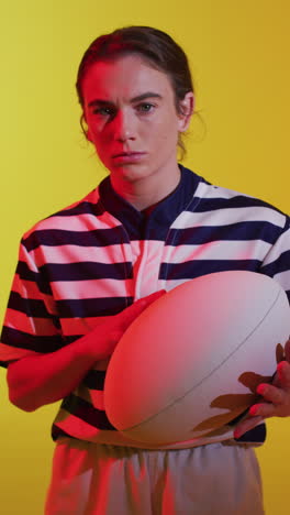 video vertical del retrato de una jugadora de rugby caucásica con una pelota de rugby sobre iluminación rosa neón