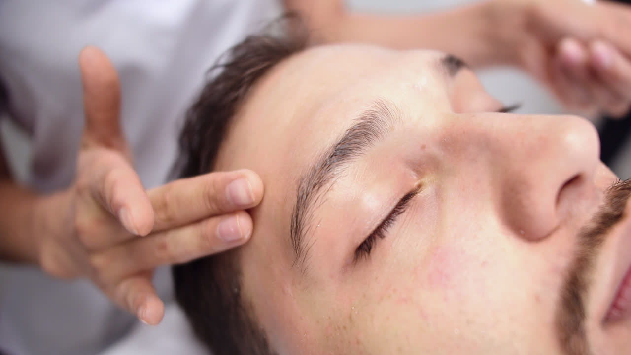 Beautiful slow motion close-up shot of a young man's face receiving massage before receiving his beauty treatment lying on a massage table in a dermatology clinic.