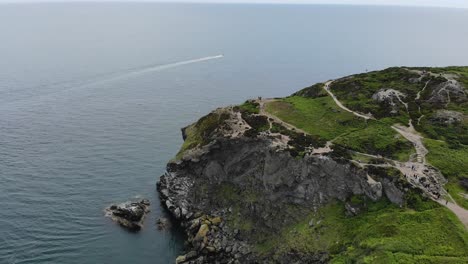 Barco-Rápido-Navegando-En-El-Océano-En-El-Mar-Irlandés-Y-Una-Gran-Montaña-Rocosa-Verde