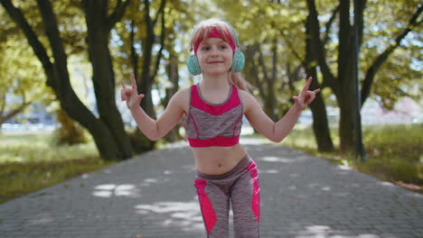 Sport-runner-child-girl-training-exercise-listening-music-on-headphones-dancing-to-camera-having-fun