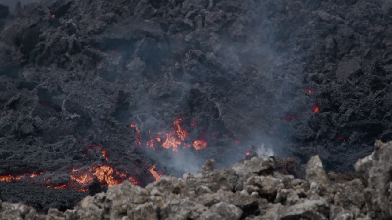 Smeltet lava, der langsomt flyder fra Grindavik vulkanen i Sundhnúkur krateret, Island, med røg der stiger op.